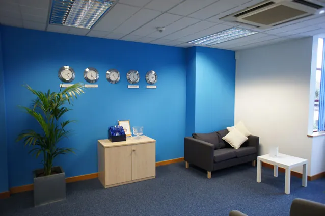 Reception area with a blue feature wall, wall clocks, a sofa and a plant